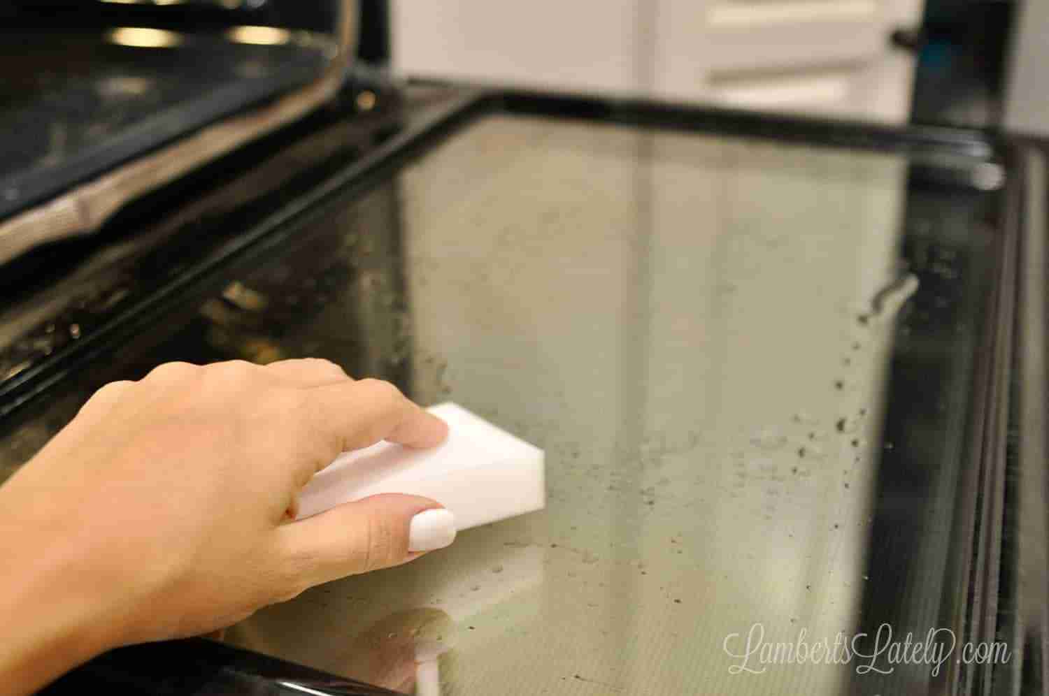 scrubbing an oven door's glass with a melamine sponge