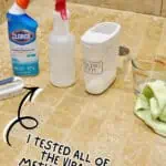 Cleaning shower grout with Clorox cleaner and spray bottles on tiled bathroom floor.