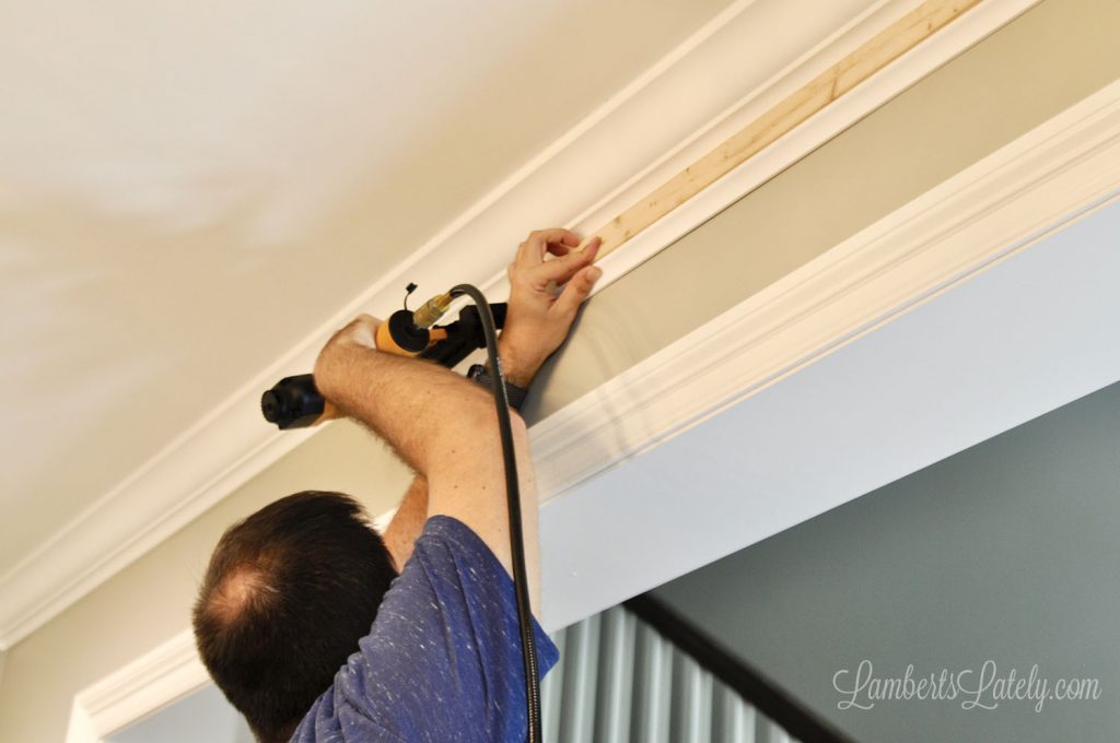 man nailing molding to a wall with a pneumatic nail gun.