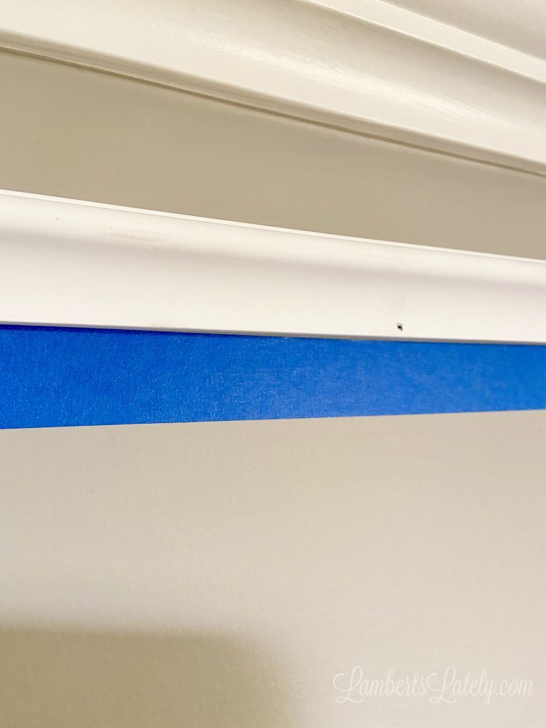 blue painters tape below molding piece on wall.