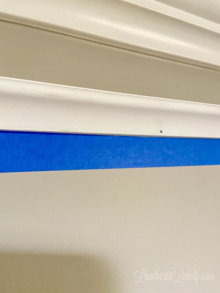 blue painters tape below molding piece on wall.