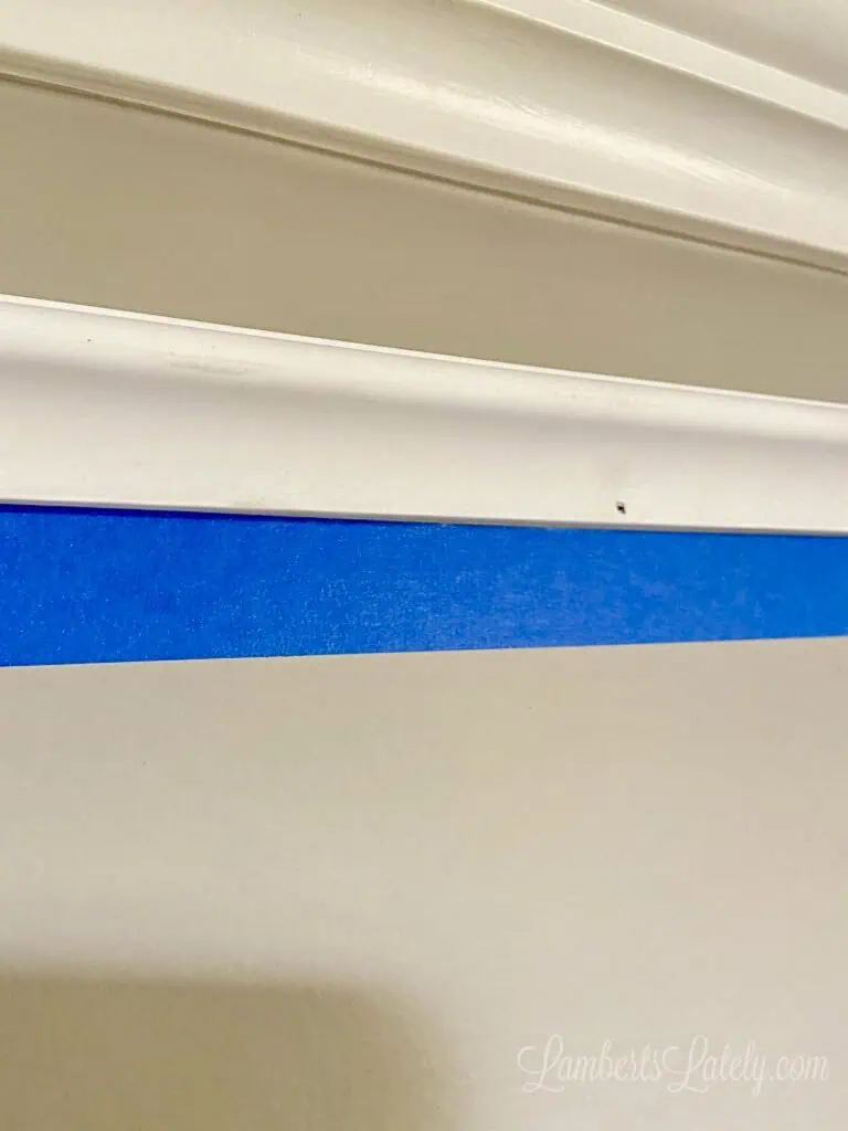 blue painters tape below molding piece on wall.