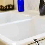 White porcelain sink with baking soda cleaning tip and blue bottle nearby.