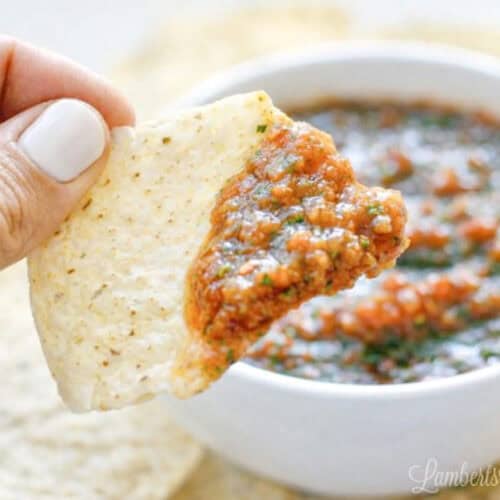 Close-up of a hand dipping a tortilla chip into salsa in a white bowl.