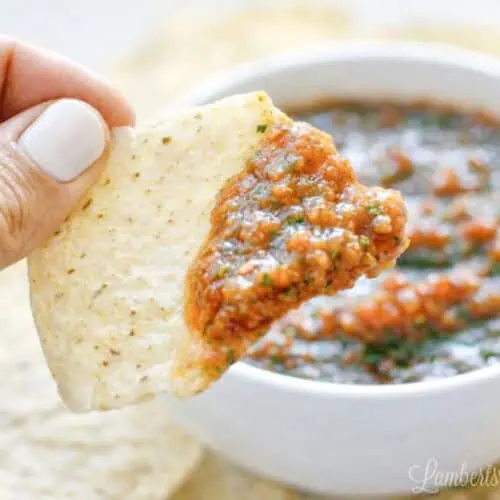 Close-up of a hand dipping a tortilla chip into salsa in a white bowl.