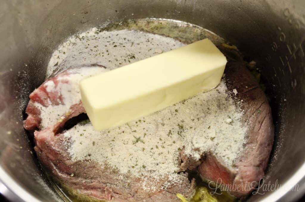 Instant Pot Mississippi Pot Roast before cooking, with butter and ranch dressing mix on top.