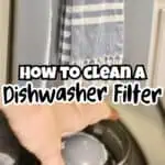 Close-up of a dishwasher filter being cleaned with a hand, towel hanging above.