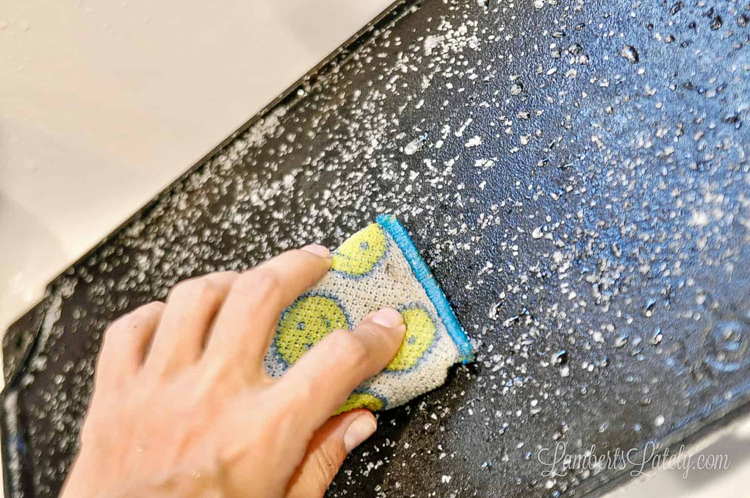 scrubbing a cast iron griddle covered in coarse salt with a scrub sponge.