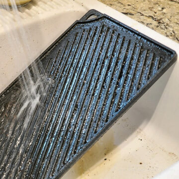 water spraying on cast iron griddle in a sink.