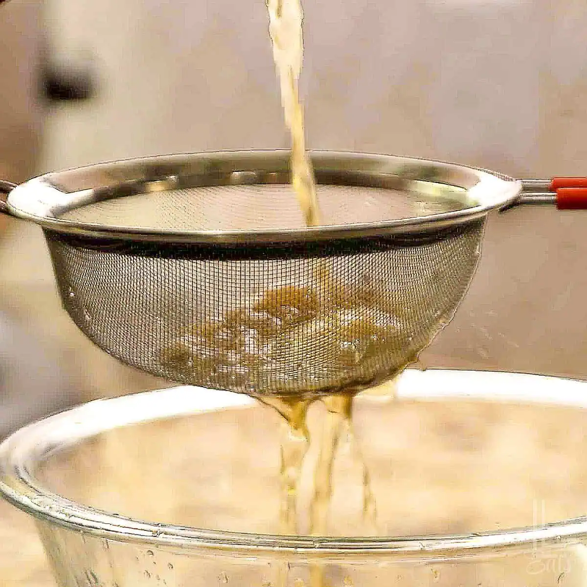 straining homemade chicken stock through a fine mesh strainer.