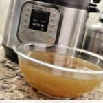 Instant Pot chicken stock in a glass bowl on a kitchen countertop.