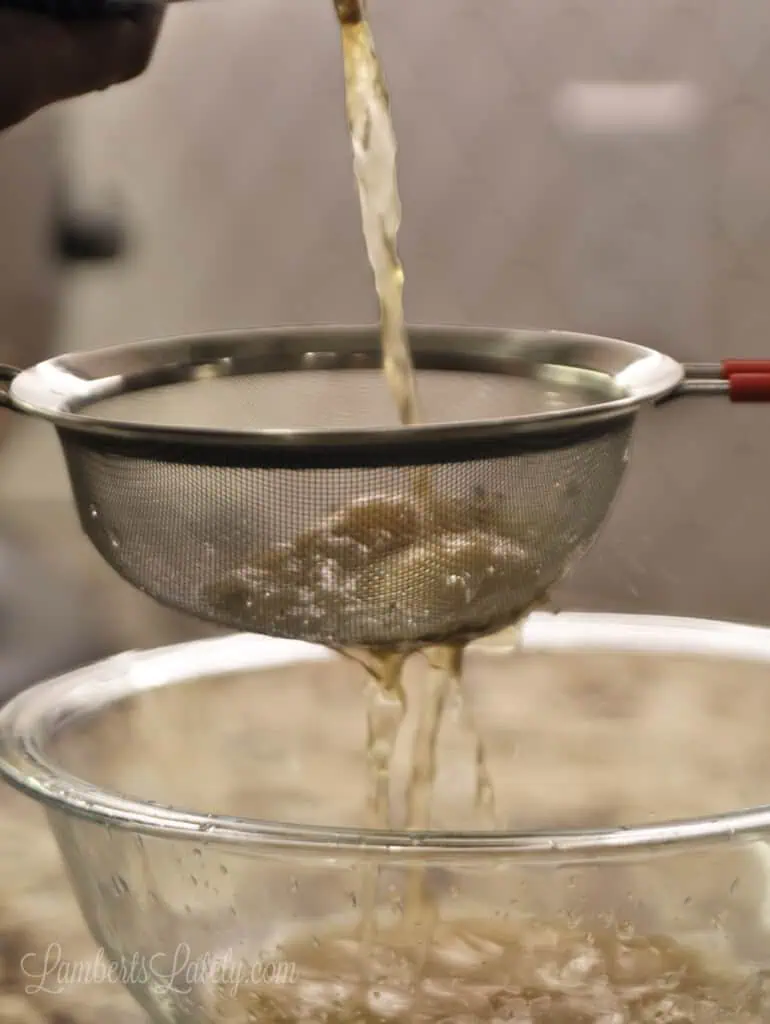 pouring chicken stock through a fine mesh strainer in front of an instant pot.
