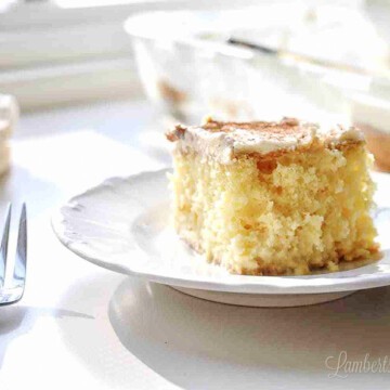 slice of tres leches cake on a plate with forks and a baking dish in background.