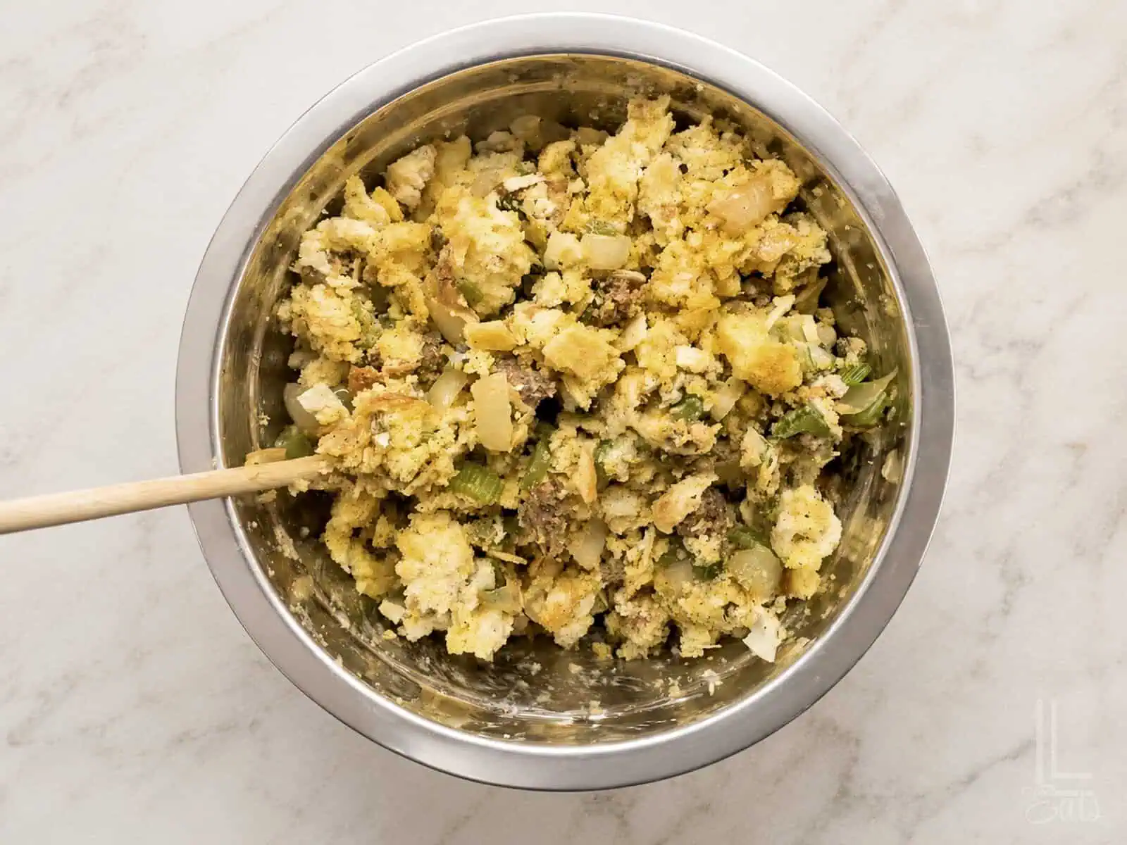 Close-up of a bowl of savory cornbread dressing with sausage and herbs being stirred together before baking.