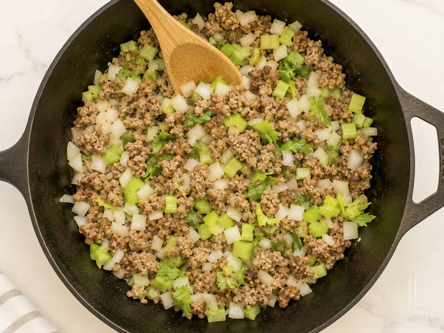 Cooking ground sausage with chopped celery and onions in a skillet for cornbread dressing.