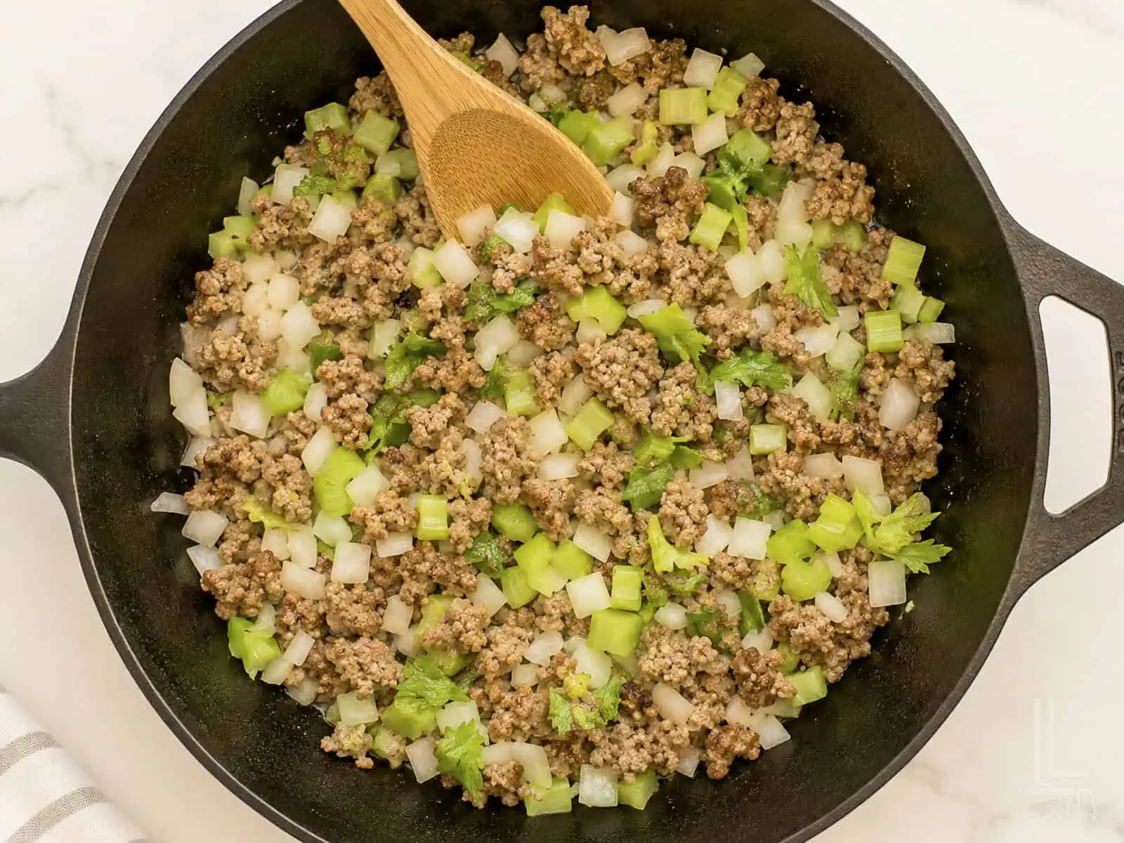 Cooking ground sausage with chopped celery and onions in a skillet for cornbread dressing.