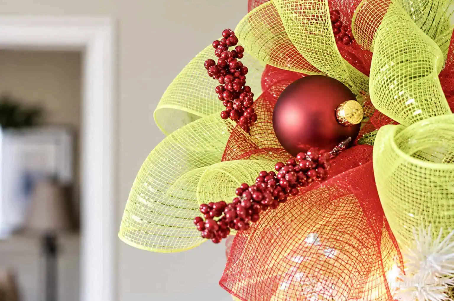 Close-up of red and green deco mesh DIY tree topper with Christmas ornaments.