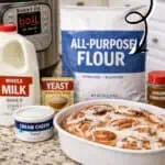 Homemade cinnamon rolls with cream cheese frosting in a baking dish, ingredients nearby.