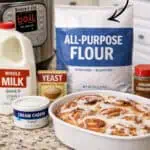 Cinnamon rolls with cream cheese frosting in a baking dish, ingredients nearby, for quick baking.