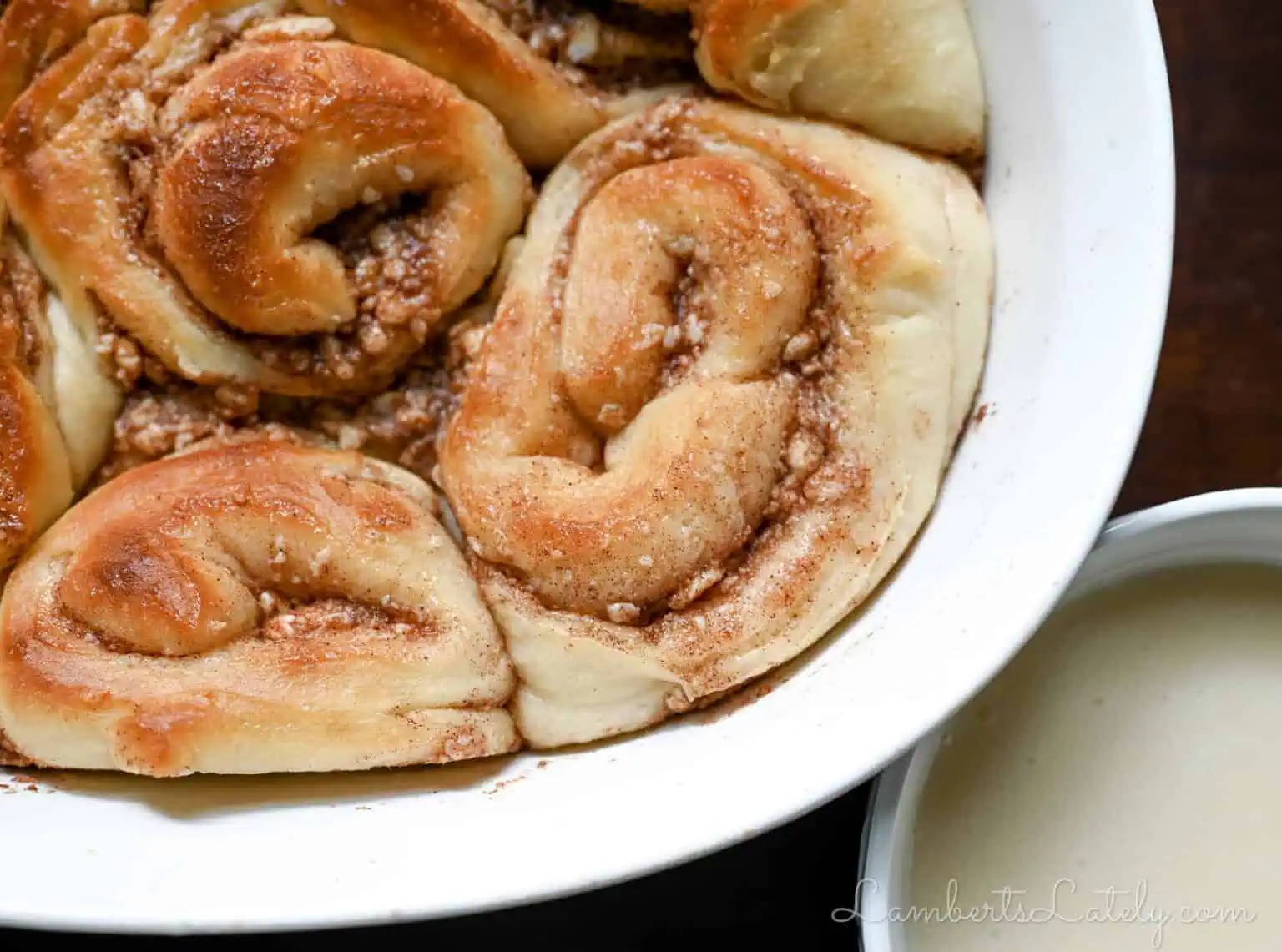 Freshly baked cinnamon rolls with cream cheese frosting in a white dish.
