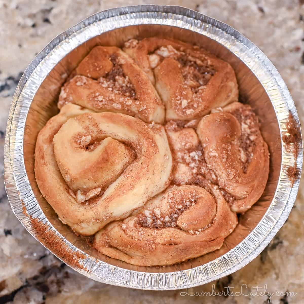 Close-up of cinnamon rolls with cream cheese frosting in a foil container.