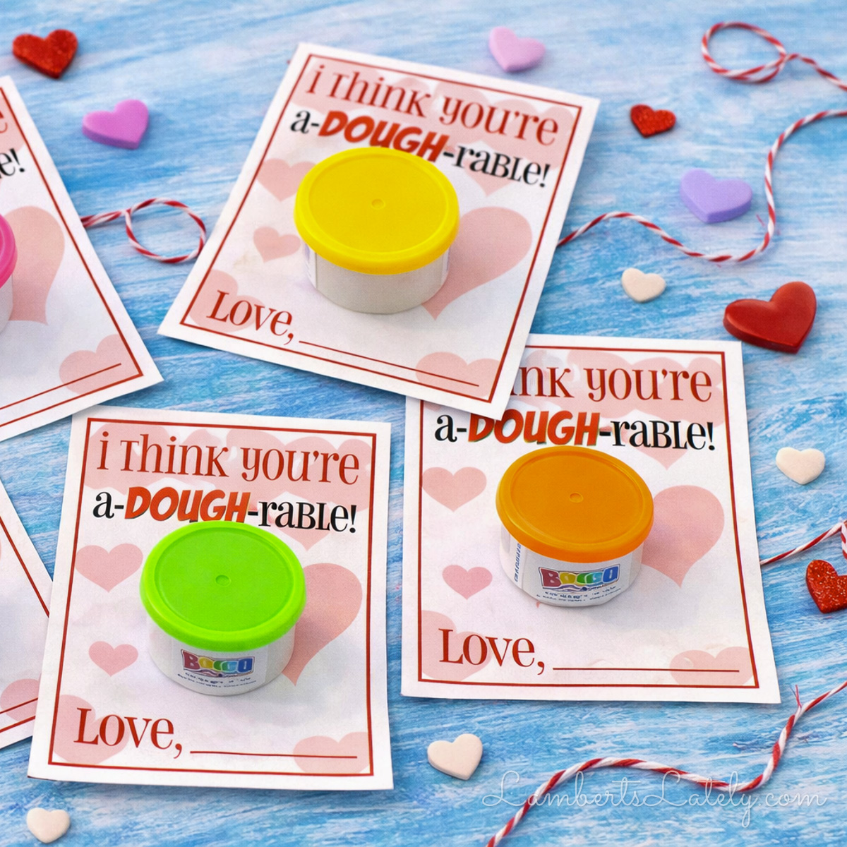 mini play dough cups attached to the play doh valentine printable cards, surrounded by string and hearts.