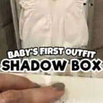 Baby's first outfit shadow box with white dress displayed in a frame.