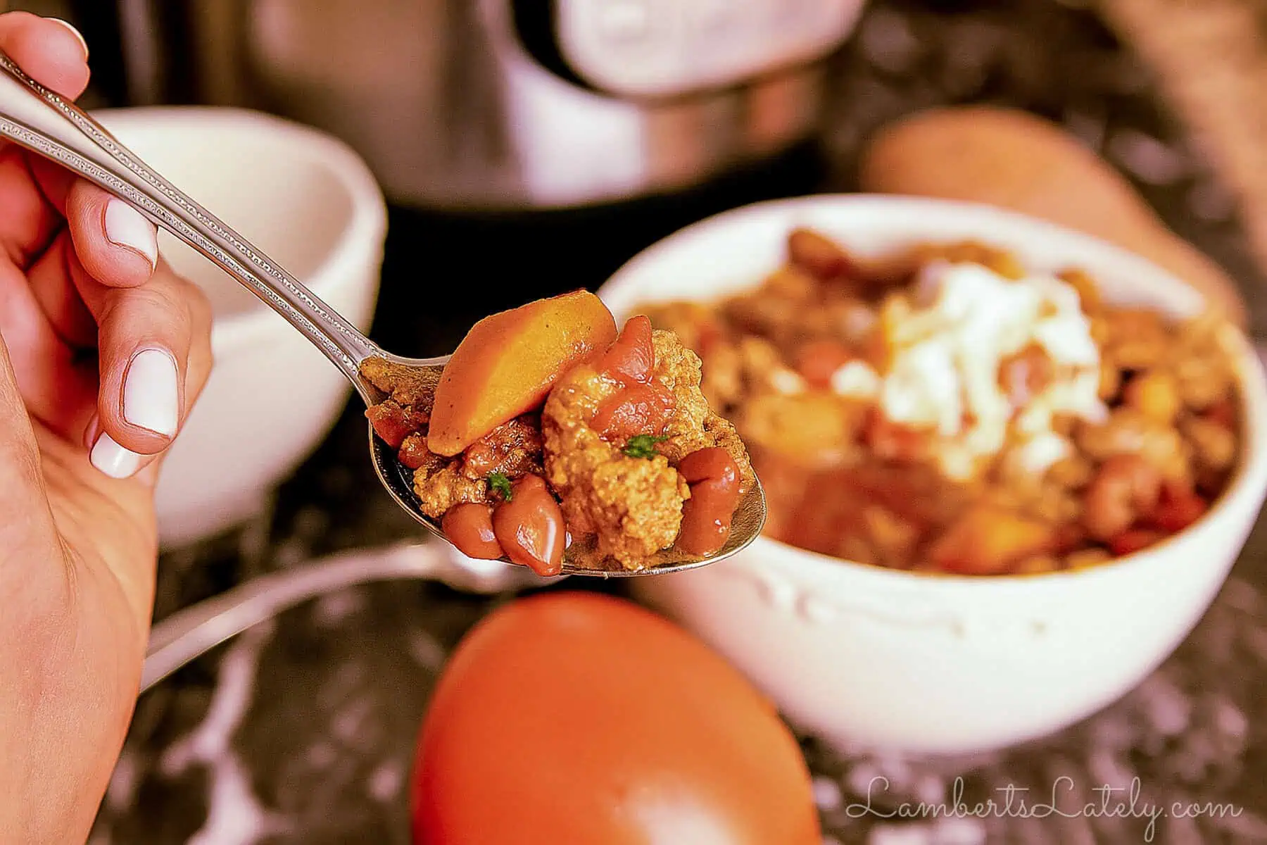 holding a spoonful of turkey chili in front of a bowl of soup and an instant pot.