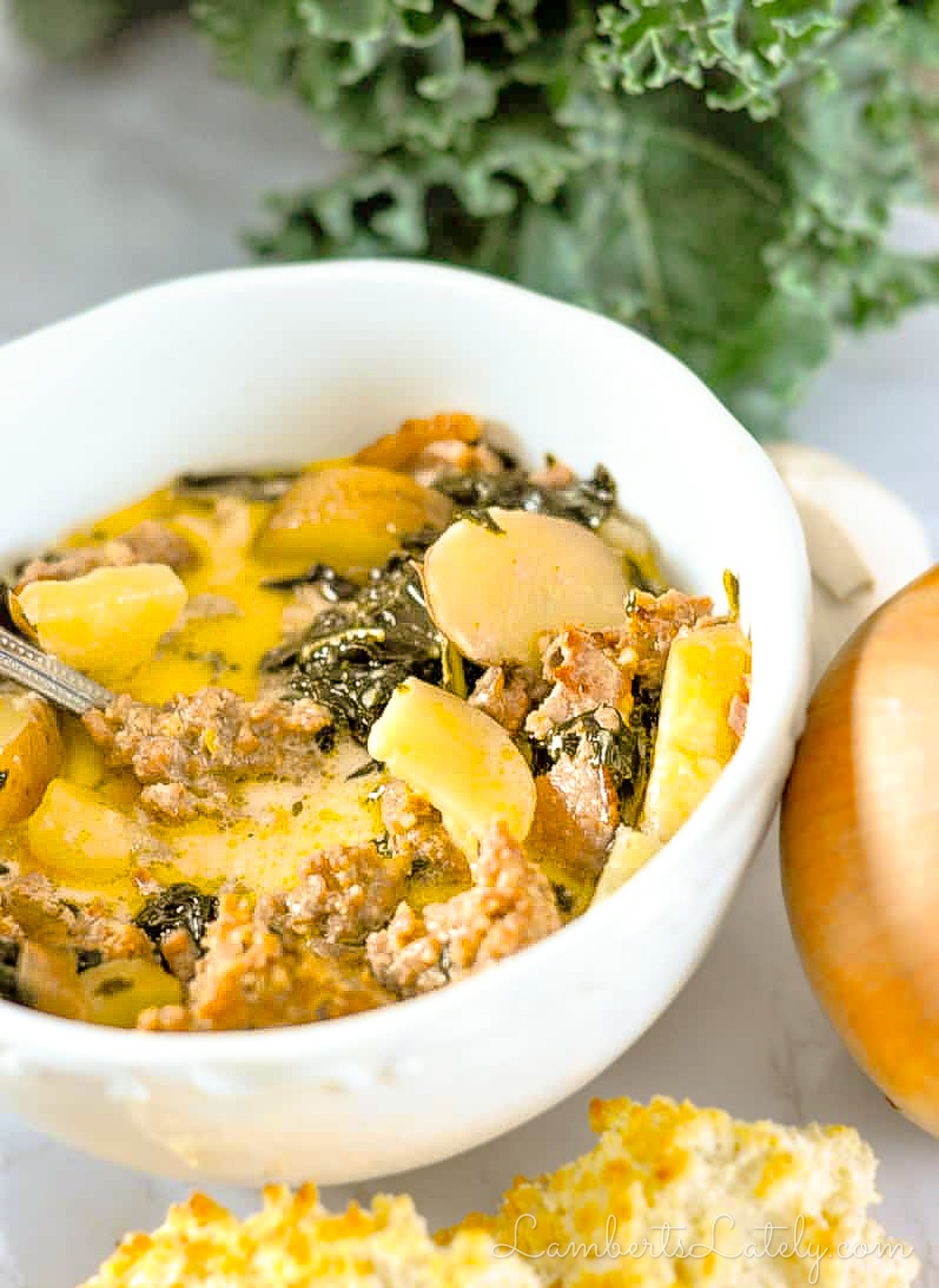 bowl of zuppa toscana soup next to onion, kale, biscuits.