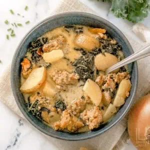 bowl of instant pot zuppa toscana, with potatoes, kale, and sausage in a creamy soup base, next to an onion, garlic, and kale.