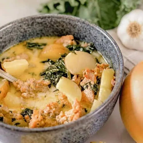 bowl of zuppa toscana with kale, potatoes, and sausage in a creamy soup.