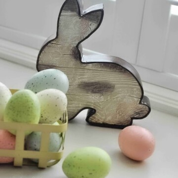 wooden easter bunny with pastel easter eggs in a yellow basket.