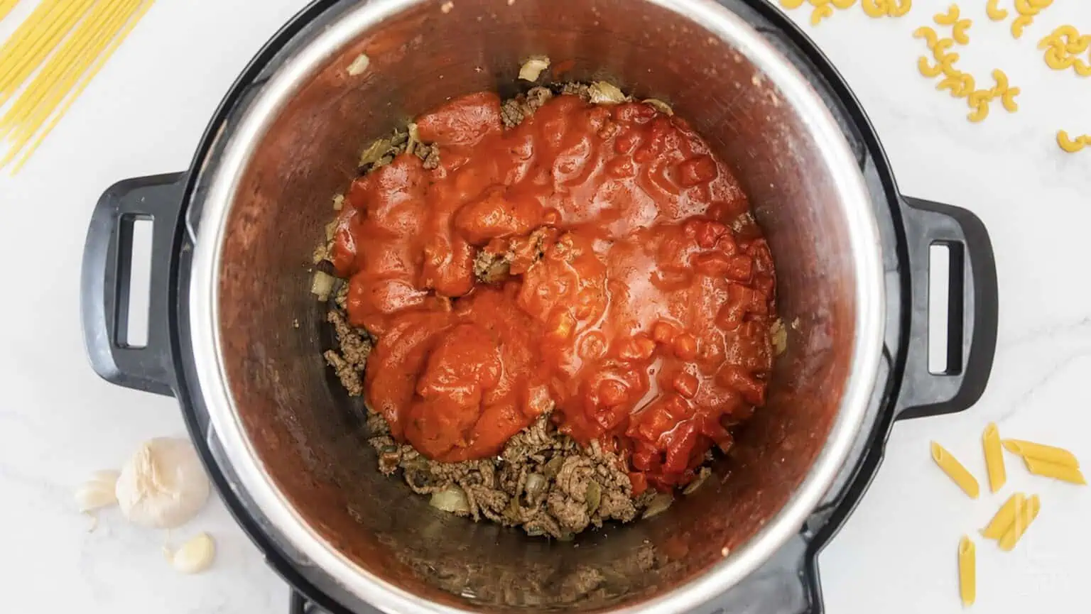 Ground beef, tomato sauce, and pasta ingredients in an Instant Pot for cooking.