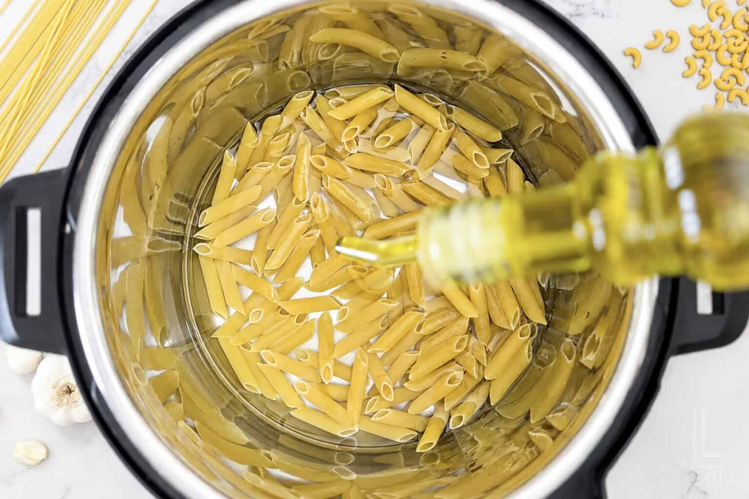 Uncooked pasta in an Instant Pot with olive oil being added.