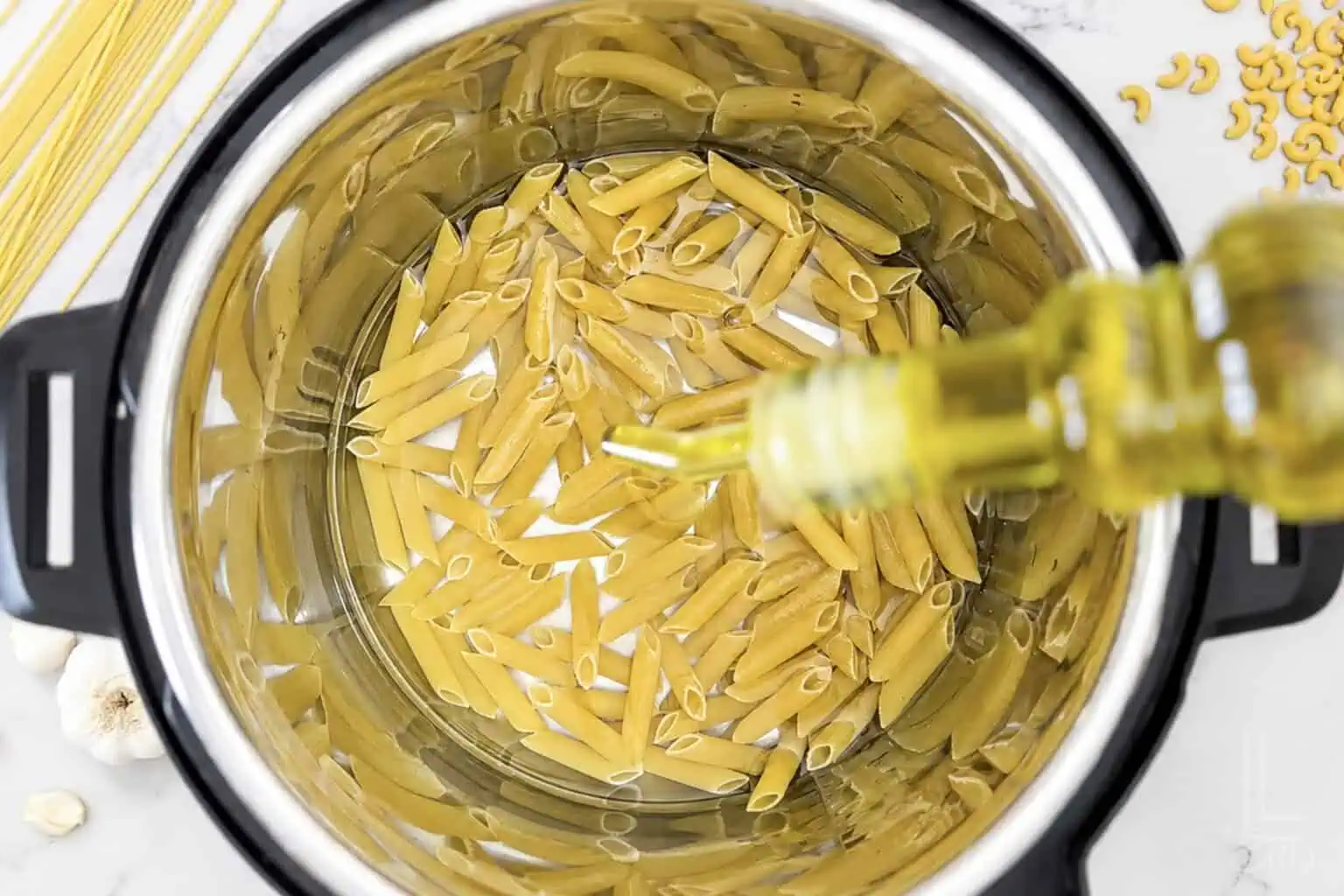Uncooked pasta in an Instant Pot with olive oil being added.