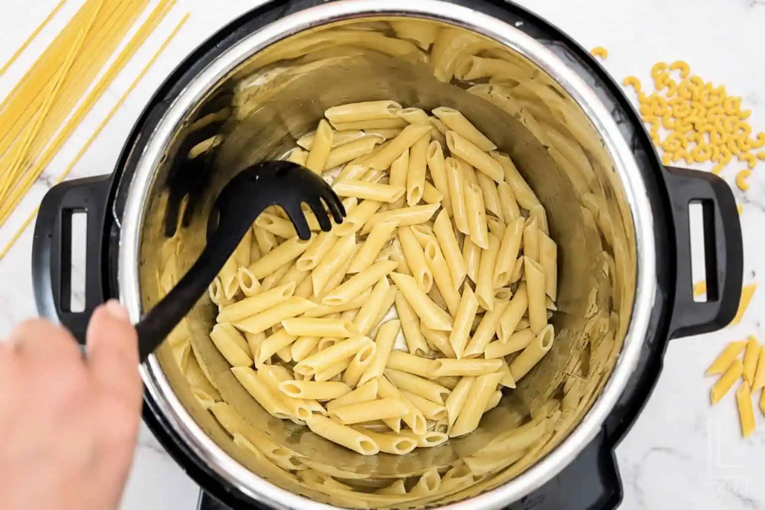 Cooked penne pasta in an Instant Pot with a black pasta fork.