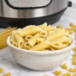a bowl of cooked penne pasta in front of an instant pot.