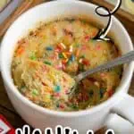 Vanilla mug cake topped with colorful sprinkles in a white mug on a wooden tray.