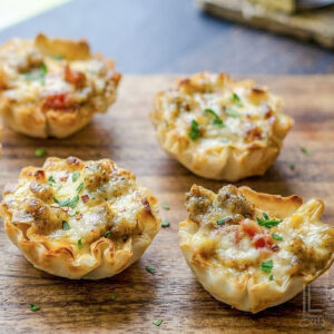 4 cheesy sausage rotel cups, with crispy phyllo shells, on a cutting board in front of a window.