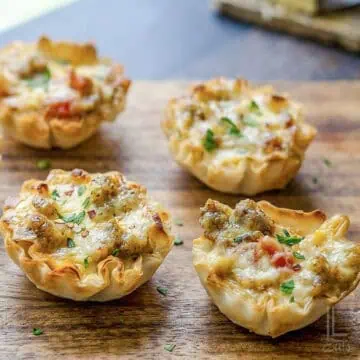 4 cheesy sausage rotel cups, with crispy phyllo shells, on a cutting board in front of a window.