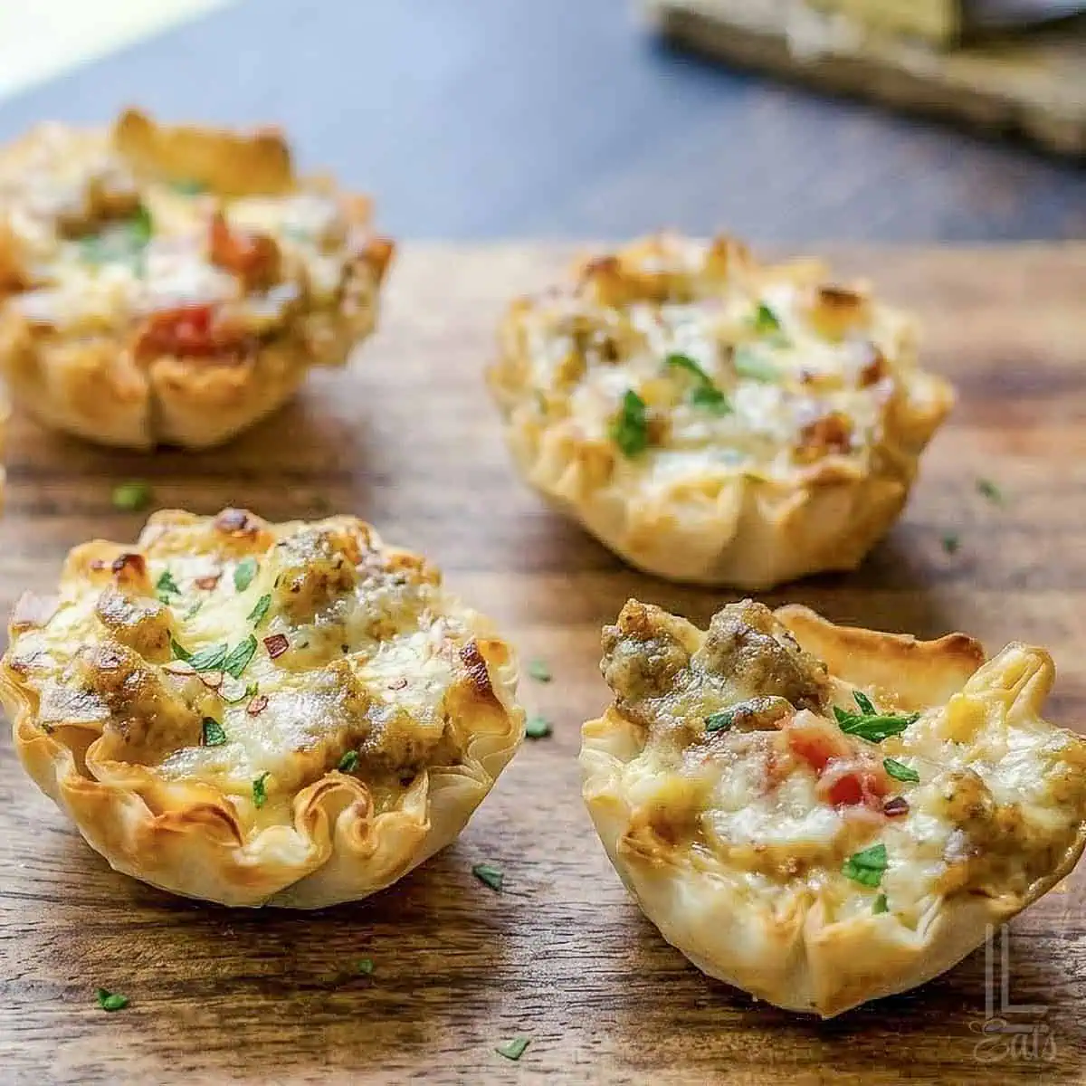 4 cheesy sausage rotel cups, with crispy phyllo shells, on a cutting board in front of a window.