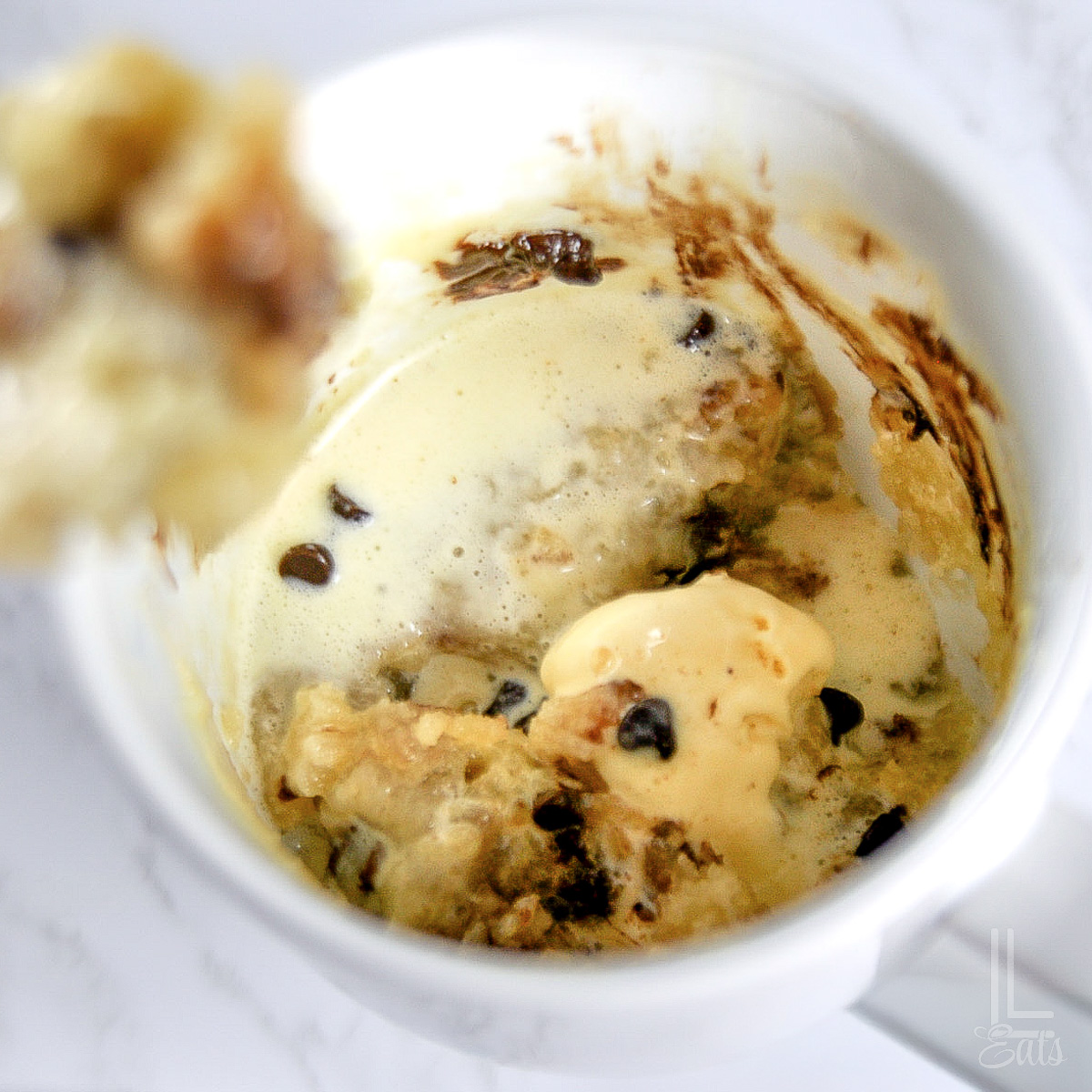 close up of gooey eggless chocolate chip mug cake in a white mug.