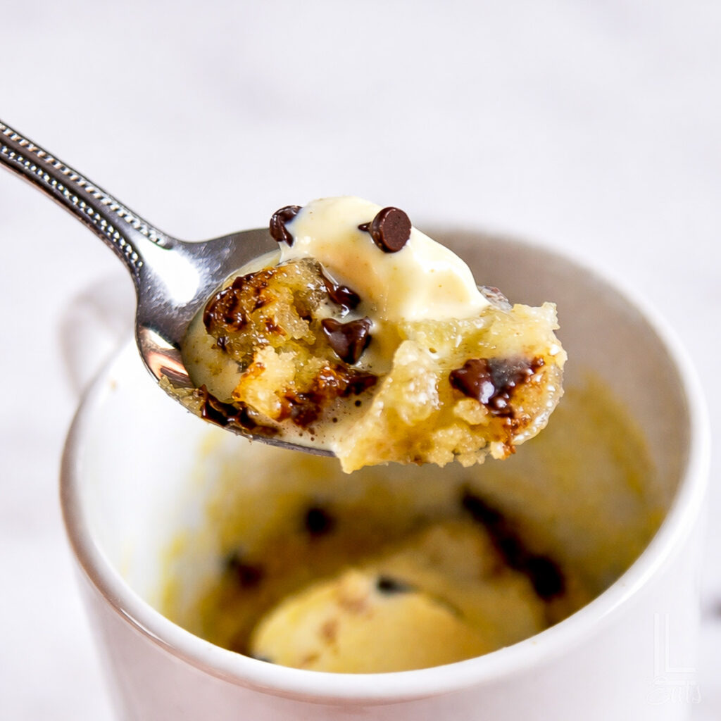 holding a spoonful of chocolate chip mug cake with ice cream in front of a mug.
