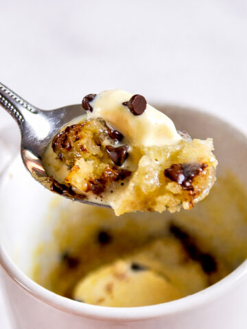 holding a spoonful of chocolate chip mug cake with ice cream in front of a mug.
