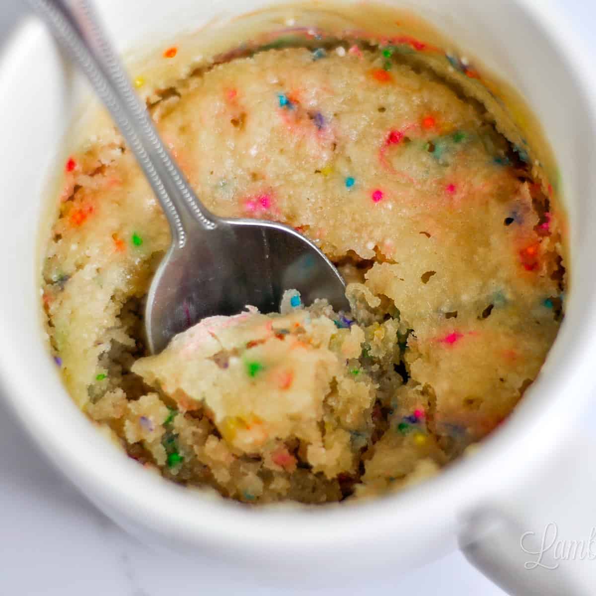 vanilla mug cake with sprinkles and a spoon.