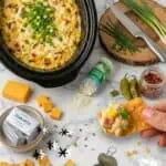 Close-up of a creamy crock pot corn dip garnished with green onions, with ingredients around.