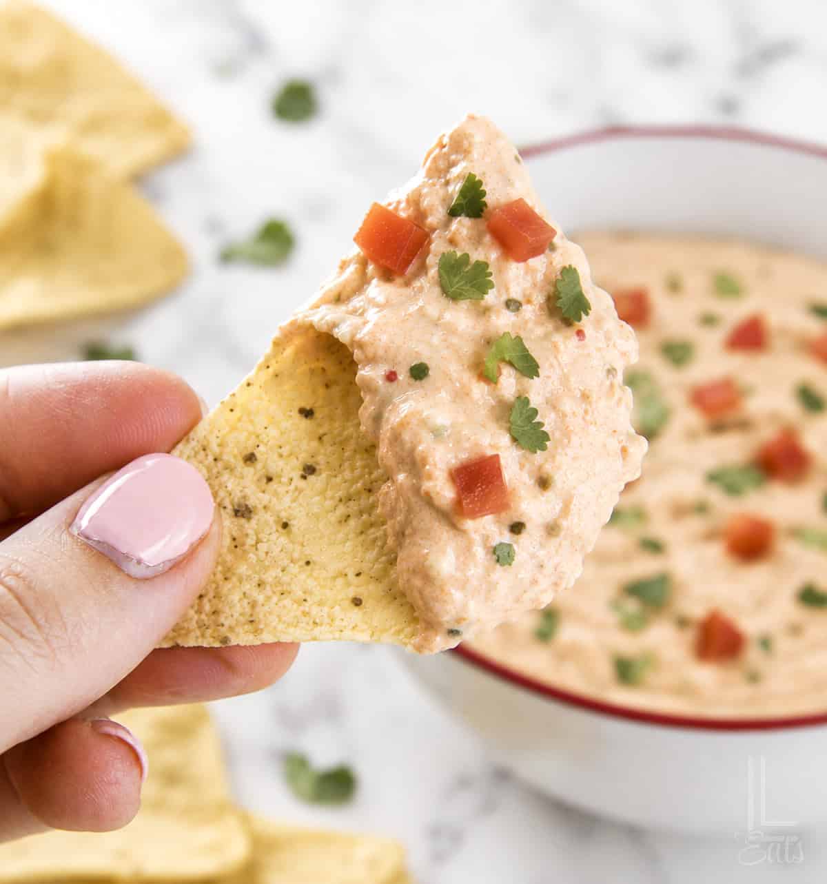 Cream cheese and salsa dip on a tortilla chip with a bowl of dip in the background.