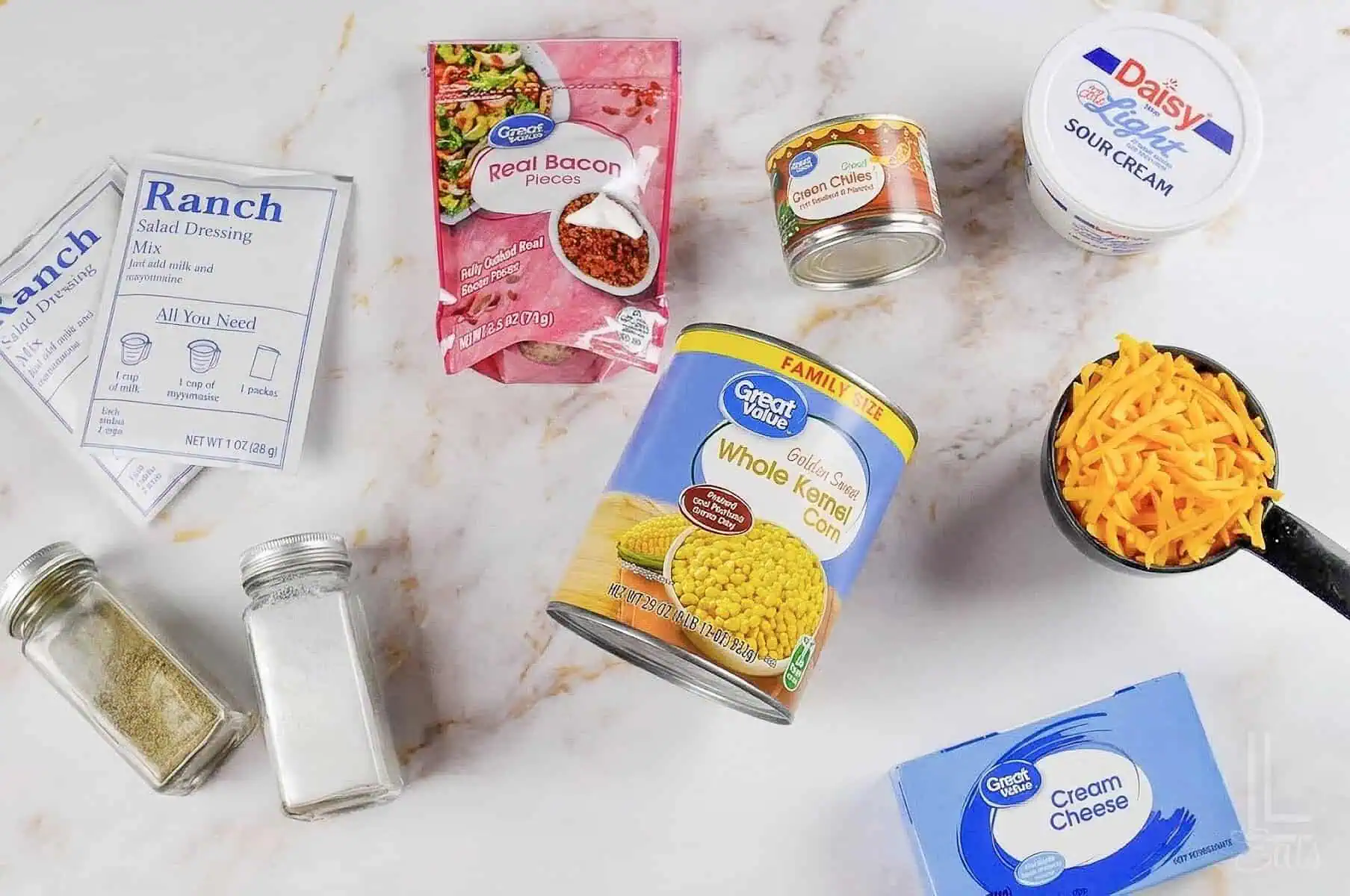 ingredients for crack corn dip, including canned corn, cheddar cheese, cream cheese, and bacon.