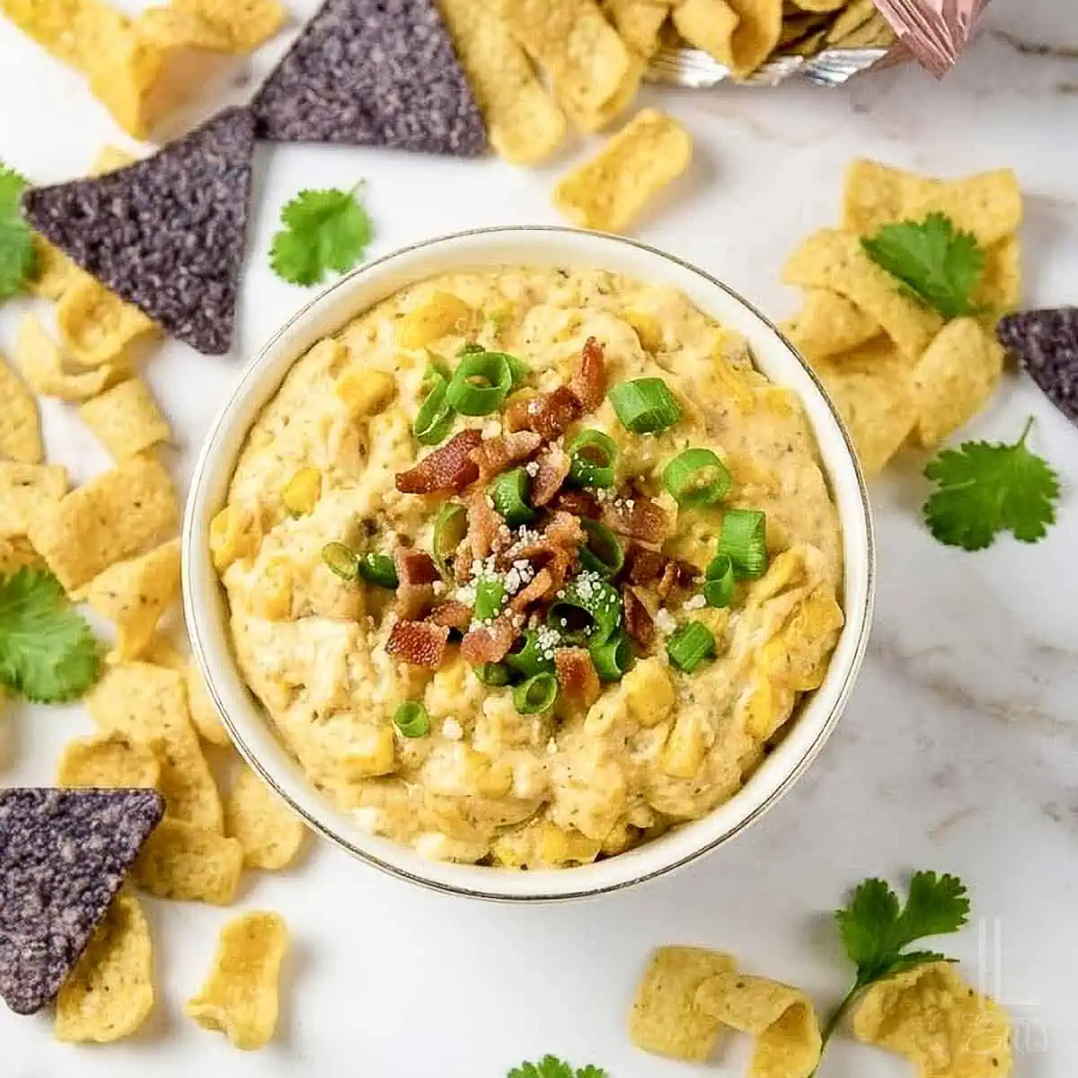 Creamy crock pot crack corn dip garnished with bacon and green onions, surrounded by chips.