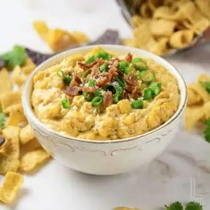 Creamy crock pot crack corn dip garnished with green onions and bacon bits.